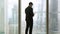 Rear view at businessman standing near full-length window using tablet