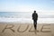 Rear view businessman standing with rule word on sand beach