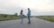 Rear view of carefree couple of teens having walk with skateboard on a road