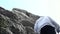 Rear view of a climber making steps towards a peak of a mountain. Footage. Man forester in hiking rubber boots climbing