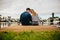 Rear view of a couple in love sitting together touching their heads near a lake. Couple on a day out sitting together holding wine