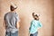 Rear view of couple with paint roller looking at wall in unrenovated room