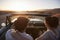 Rear View Of Couple On Road Trip Driving Classic Convertible Car Towards Sunset