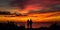 Rear view of a couple watching a stunning summer sunset, their silhouettes outlined against the colorful sky, concept of
