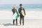 Rear view of couple in wetsuit with surfboard standing on the beach