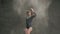 Rear View of a dancer girl who moving in cloud of white dust or powder on gray background at studio. Female ballet