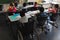 Rear view of disable schoolboy with classmate studying and sitting at desk in classroom