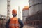 Rear view of engineer standing in front of oil refinery plant. An engineers rear view wearing a safety helmet in construction site