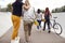 Rear View Of Female Friends With Skateboards And Bike Walking Through Urban Skate Park