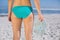 Rear view of fit woman in bikini on beach holding flip flops