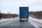 Rear view at freight truck driving on slippery winter highway, northern forest route, blured roadside