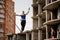 Rear view girl walking on the slackline rope to the unfinished buildings