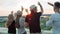 Rear view group of people enjoying beautiful city landscape raising arms on rooftop party at sunset