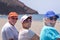 Rear view of group of three friends sitting on the beach, retired adult people in outdoor vacation at sea smiling enjoying sun and