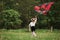 Rear view. Happy girl in casual clothes running with kite in the field. Beautiful nature