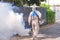 Rear view of healthcare worker spraying chemical to eliminate mosquitoes on street in alley of public suburb community