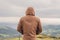 Rear view of hipster man in hood standing and watching sea and hill landscape panorama