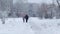 Rear view of hooded female person with child walking the city street in cold winter afternoon. Clip. Gray dull urban