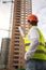 Rear view image of male architect pointing at buildings under construction with roll of blueprints