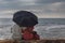 Rear View of Indian couple sitting by sea with an umbrella looking at horizon.