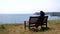 Rear view of lone woman sitting on the bench on seaside
