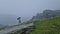 Rear view of a lonely man with umbrella stands on a rocky hill covered by haze. Moody and emotional scene with a lone stranger