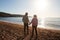 Rear View Of Loving Retired Couple Holding Hands Looking Out To Sea On Winter Beach Vacation