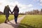 Rear View Of Loving Senior Couple Holding Hands Enjoying Autumn Or Winter Walk Through Park Together