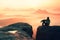 Rear view of male hiker sitting on the rocky peak while enjoying a colorful daybreak above mounrains valley