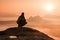 Rear view of male hiker sitting on the rocky peak while enjoying a colorful daybreak above mounrains valley