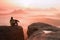 Rear view of male hiker sitting on the rocky peak while enjoying a colorful daybreak above mounrains valley