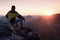 Rear view of male hiker in yellow black jacket sitting on rocky cliff while enjoying daybreak above valley