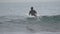 Rear view male surfer athlete wearing in black wetsuit lying on front on surfboard cruising along breaking wave in