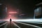 Rear view of man in black coat and hat standing in rain on city street at night.