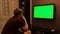 Rear view of man looking at green TV. Concept. Man watches TV with green screen and presses remote control. Man switches