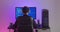 Rear view of man programmer in headphones coding network security software indoors in neon lights at night. Hacker