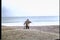 Rear view of man walking down beach with fishing rods