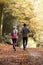 Rear View Of Mature Couple Running Through Autumn Woodland