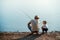 A rear view of mature father with a small toddler son outdoors fishing by a lake.