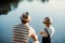 A rear view of mature father with a small toddler son outdoors fishing by a lake.