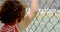 Rear view of mixed-race schoolgirl standing near wire mesh fence at school 4k