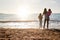 Rear View Of Mother With Daughters Looking Out To Sea Silhouetted Against Sun