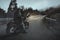 Rear view of muscular man, professional biker in leather outfit sitting on bike at suburban highway in evening. Concept