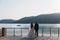 Rear view newlyweds couple, bride and groom holding hands on a lake background. Cute girl in white dress, men in black