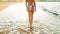 Rear view photo of beautiful young barefoot woman with perfect body wearing bikini walking on the sandy sea beach