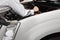 Rear view of professional young mechanic man in uniform with wrench diagnosing engine against car in open hood at the repair garag