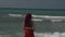 Rear view of a red-haired young woman in sunglasses stands in a strip of sea surf