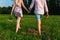 Rear view of a romantic man and woman stand on walk on field grass. Concept of lovely family holding hands. Young couple running t