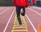 Rear view of runner running over six in plastic yellow hurdles on a track