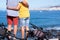 Rear view of senior couple hugging standing on the cliff in sea excursion with their bicycles, horizon on the sea. Active retirees